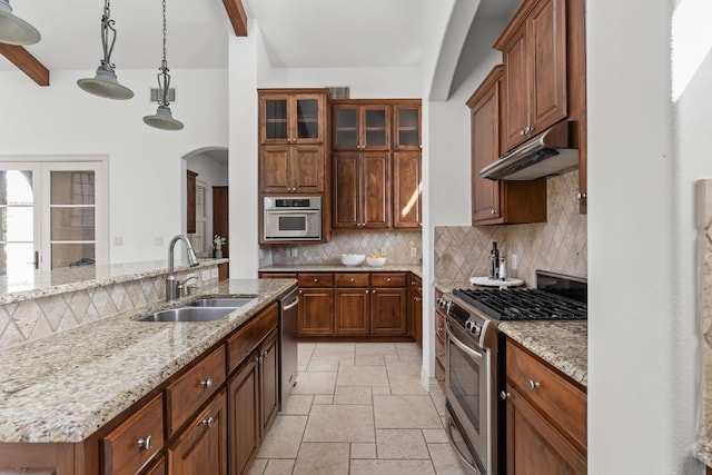 kitchen with stone tile floors, a sink, decorative backsplash, under cabinet range hood, and appliances with stainless steel finishes