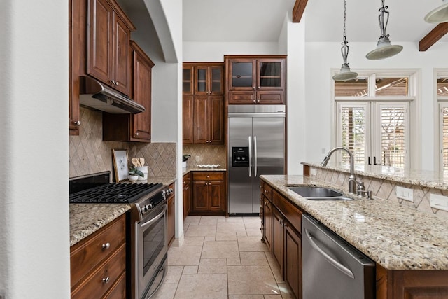 kitchen featuring stone tile floors, a sink, under cabinet range hood, appliances with stainless steel finishes, and backsplash