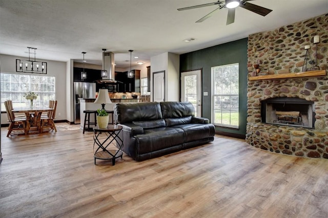 living area with ceiling fan with notable chandelier, a fireplace, baseboards, and light wood-style floors