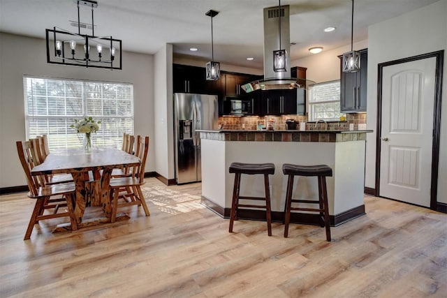 kitchen with plenty of natural light, backsplash, an inviting chandelier, and stainless steel refrigerator with ice dispenser