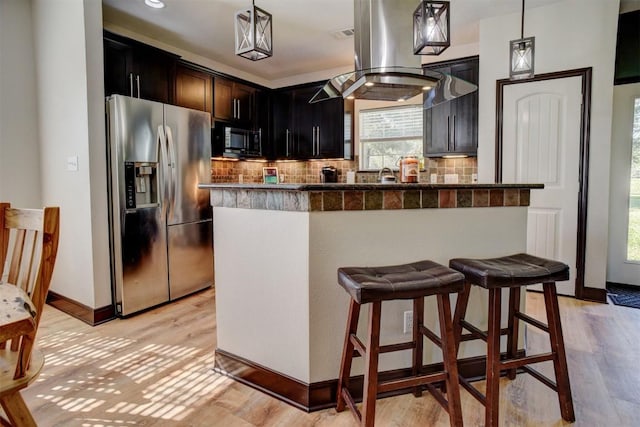 kitchen with a breakfast bar area, island exhaust hood, stainless steel fridge with ice dispenser, light wood-style floors, and tasteful backsplash