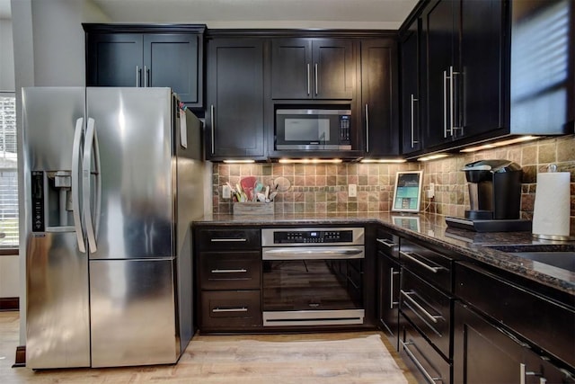 kitchen with tasteful backsplash, stainless steel appliances, light wood-style floors, and dark stone counters