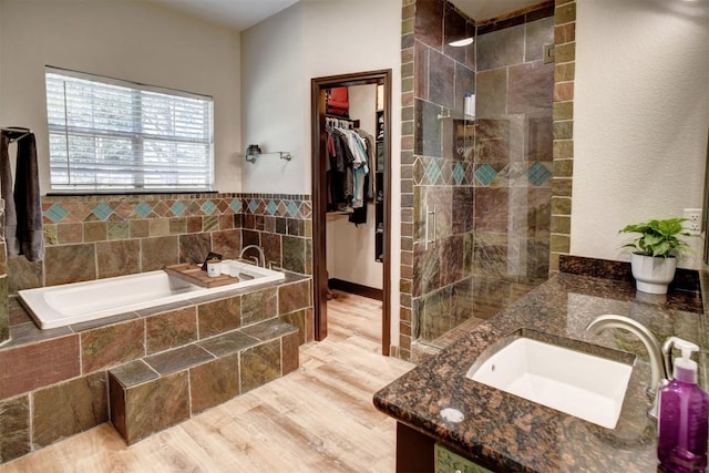 bathroom featuring a walk in closet, a garden tub, tiled shower, wood finished floors, and a sink