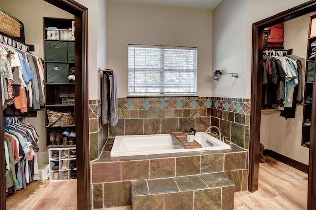 bathroom featuring baseboards, a garden tub, wood finished floors, and a spacious closet