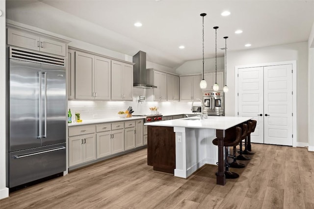 kitchen featuring stainless steel appliances, wall chimney range hood, a sink, backsplash, and light countertops