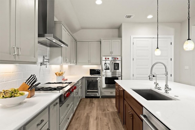 kitchen with wall chimney range hood, stainless steel appliances, a sink, light countertops, and light wood-style floors