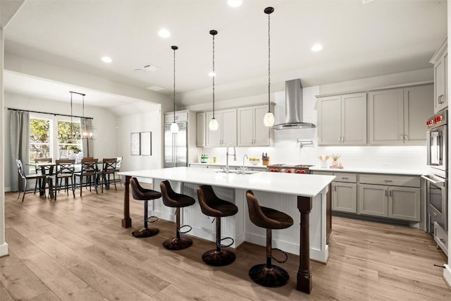kitchen with wall chimney range hood, stainless steel appliances, recessed lighting, light countertops, and light wood-style floors
