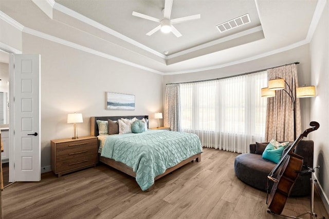 bedroom featuring visible vents, ornamental molding, a tray ceiling, wood finished floors, and ceiling fan