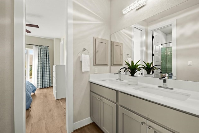 bathroom with wood finished floors, double vanity, a shower with door, baseboards, and a ceiling fan
