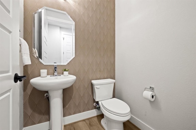 half bathroom with wood finished floors, baseboards, and toilet