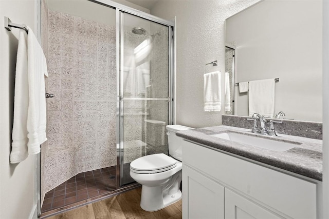 bathroom with toilet, wood finished floors, a shower stall, vanity, and a textured wall