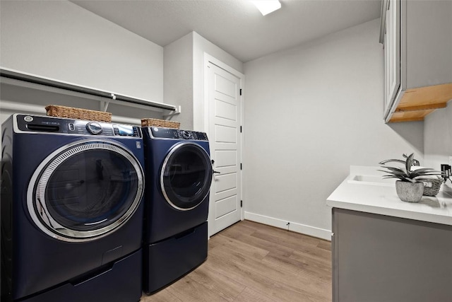 laundry room featuring baseboards, cabinet space, a sink, washing machine and dryer, and light wood-type flooring