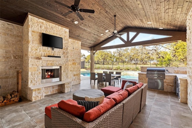 view of patio featuring area for grilling, an outdoor living space with a fireplace, fence, exterior kitchen, and ceiling fan