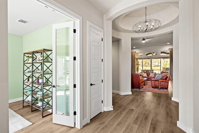 hall with visible vents, a notable chandelier, wood finished floors, arched walkways, and baseboards