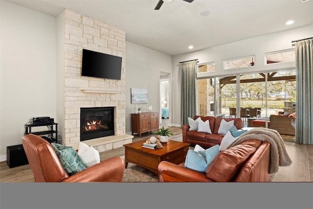 living area featuring a fireplace, baseboards, a ceiling fan, and wood finished floors