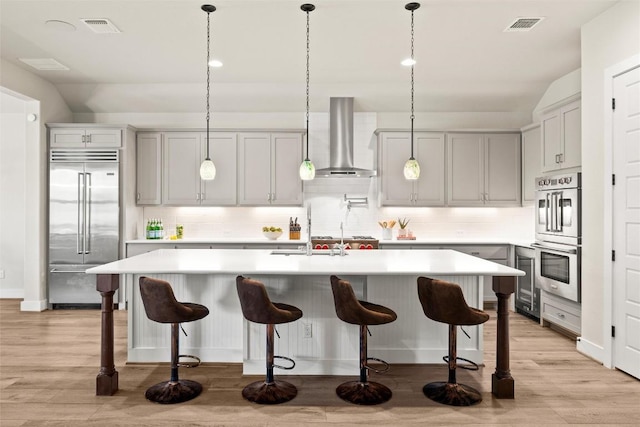 kitchen with stainless steel appliances, wall chimney range hood, tasteful backsplash, light countertops, and a sink