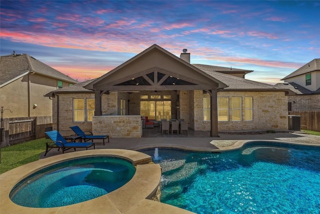 back of property at dusk with stone siding, a patio area, a chimney, and a fenced backyard