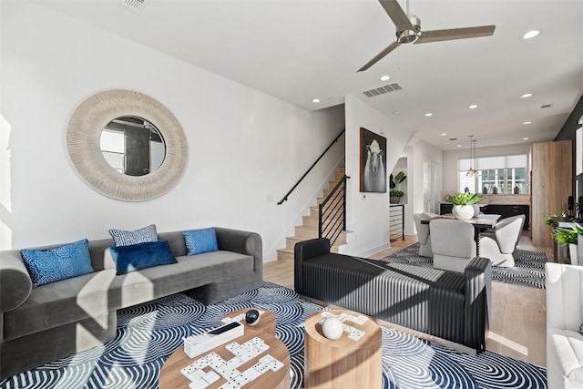 living room featuring stairway, a ceiling fan, visible vents, light wood finished floors, and recessed lighting