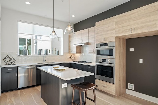 kitchen featuring backsplash, a kitchen island, light countertops, appliances with stainless steel finishes, and a sink