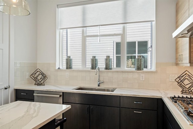 kitchen featuring under cabinet range hood, stainless steel gas cooktop, light stone counters, decorative backsplash, and a sink