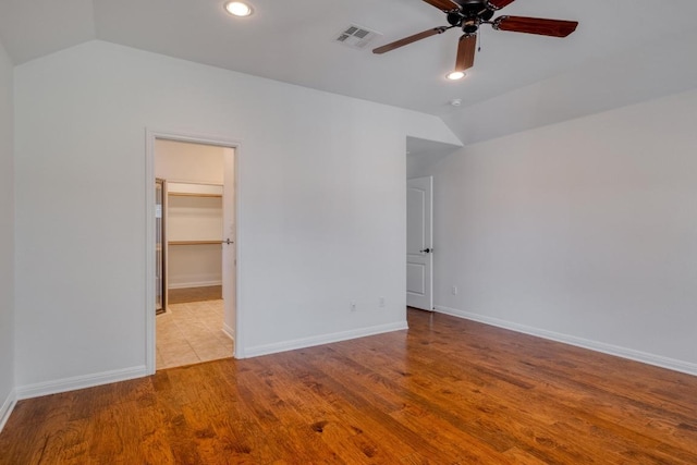 unfurnished bedroom featuring a spacious closet, visible vents, baseboards, vaulted ceiling, and wood finished floors