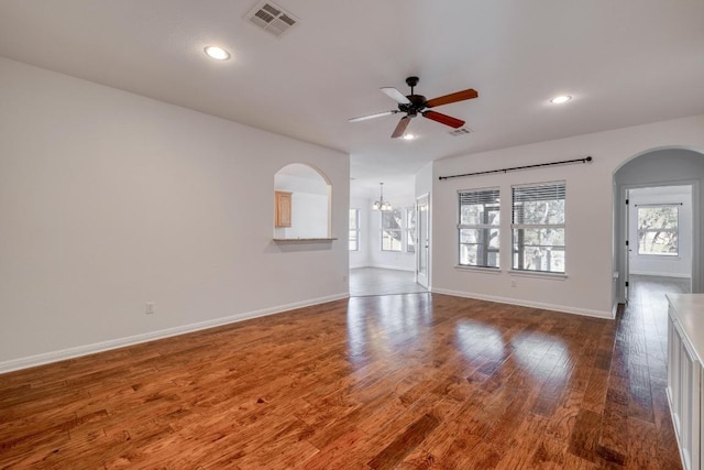 unfurnished living room featuring arched walkways, visible vents, plenty of natural light, and wood finished floors