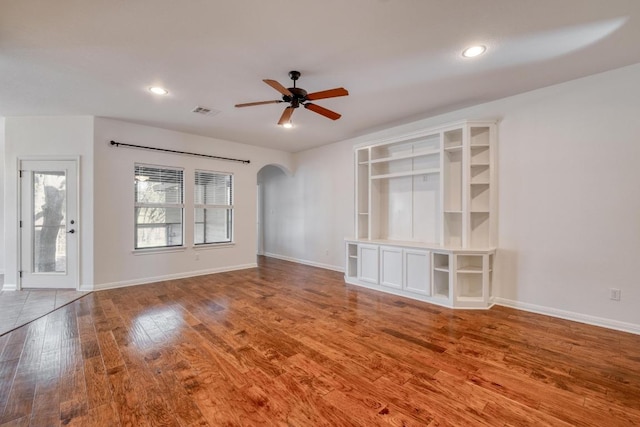 unfurnished living room featuring visible vents, baseboards, ceiling fan, wood finished floors, and arched walkways