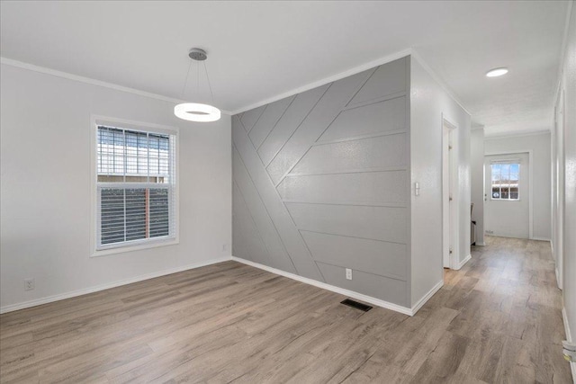 spare room featuring light wood finished floors, visible vents, baseboards, and ornamental molding