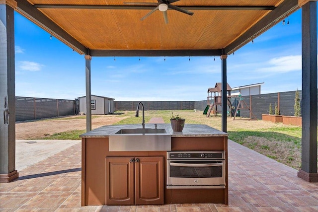 view of patio / terrace featuring a playground, a storage shed, a fenced backyard, an outbuilding, and a sink