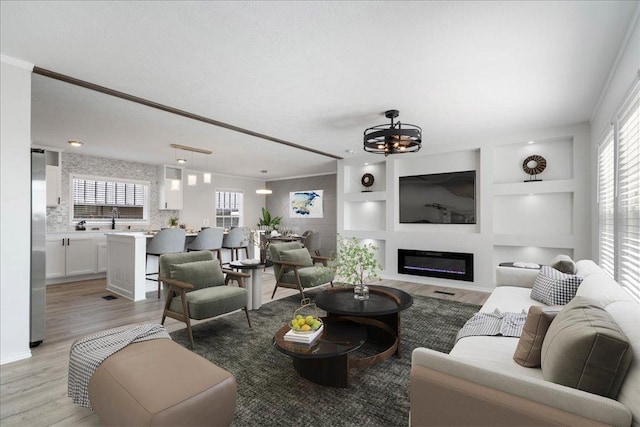 living room with a glass covered fireplace, an inviting chandelier, built in features, and light wood finished floors