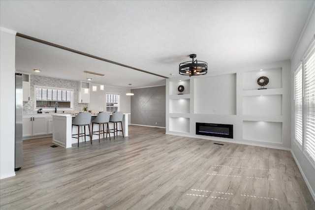 living area with a glass covered fireplace, built in features, baseboards, and light wood finished floors