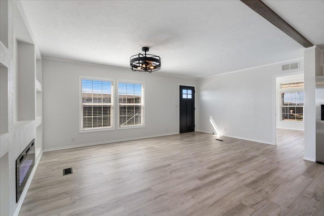 unfurnished living room featuring a glass covered fireplace, a notable chandelier, light wood-style floors, and visible vents