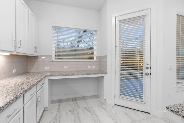 kitchen featuring white cabinetry, marble finish floor, light stone countertops, and built in study area