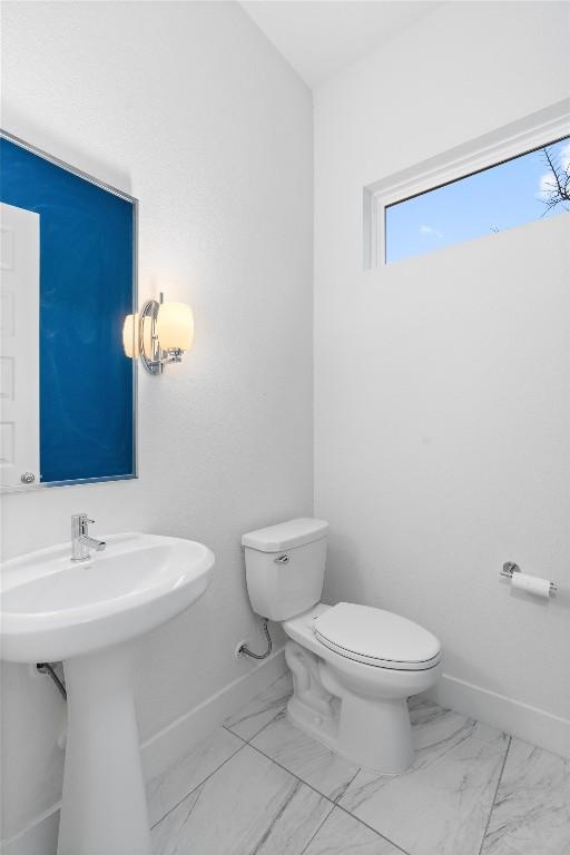 bathroom with baseboards, toilet, and marble finish floor