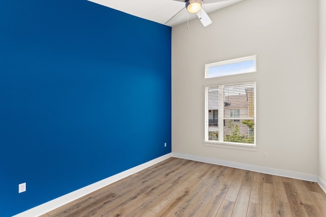 spare room featuring hardwood / wood-style floors, a high ceiling, a ceiling fan, and baseboards