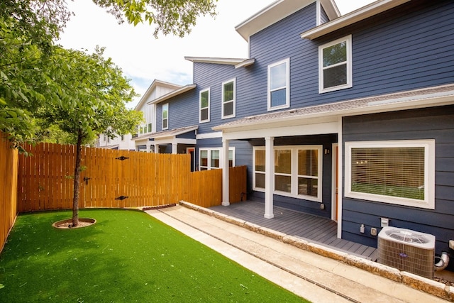 rear view of house featuring fence, a lawn, and central AC