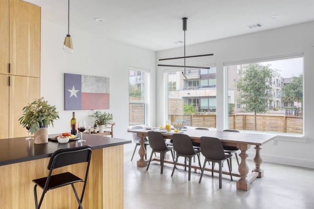 dining space with a wealth of natural light, visible vents, baseboards, and concrete flooring