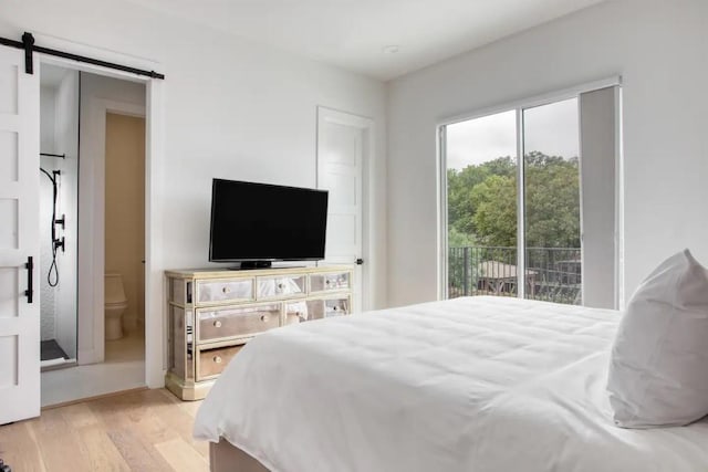 bedroom featuring access to exterior, light wood finished floors, ensuite bathroom, and a barn door