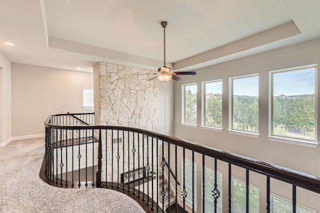 hall with a tray ceiling, baseboards, an upstairs landing, and carpet flooring