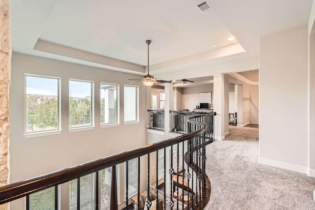 corridor with visible vents, an upstairs landing, baseboards, carpet, and a raised ceiling