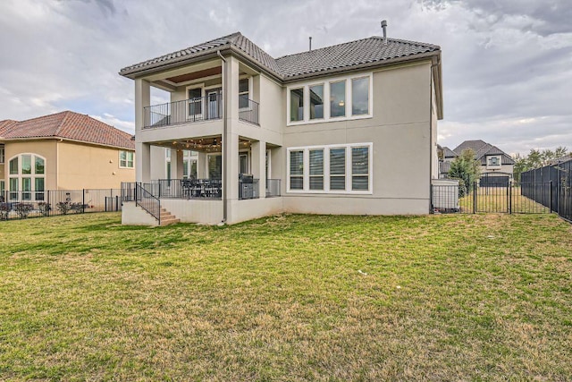 back of property with a yard, a balcony, a fenced backyard, and stucco siding