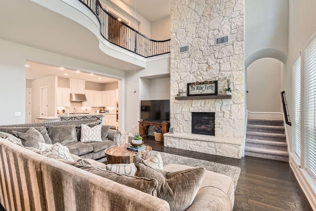 living room featuring a stone fireplace, dark wood-type flooring, stairway, and visible vents