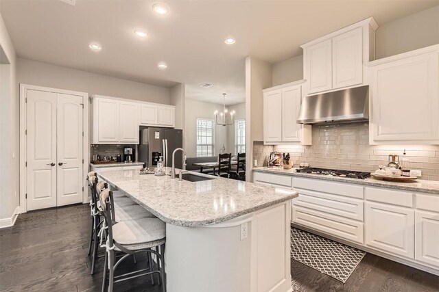 921 Morning Moon Cir, Austin, TX 78732 - kitchen featuring stainless steel appliances, under cabinet range hood, dark wood finished floors, a kitchen island with sink, and decorative backsplash
