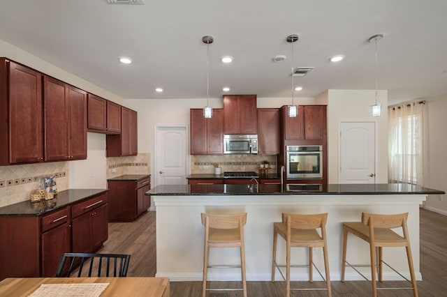 kitchen with dark countertops, visible vents, a spacious island, appliances with stainless steel finishes, and wood finished floors