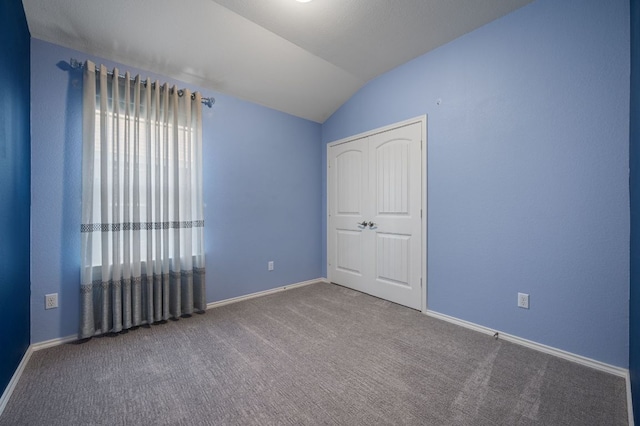 carpeted spare room featuring lofted ceiling and baseboards