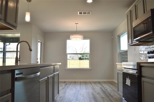 kitchen featuring visible vents, baseboards, decorative light fixtures, light wood-style floors, and stainless steel appliances