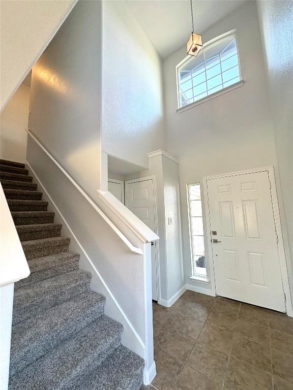 tiled foyer entrance featuring stairs, baseboards, and a towering ceiling