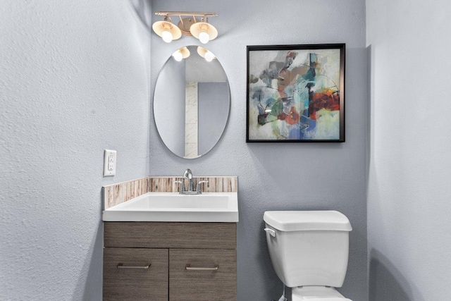 half bath featuring vanity, toilet, and a textured wall