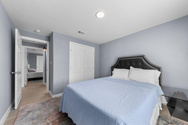 bedroom featuring light wood-type flooring, visible vents, baseboards, and a closet