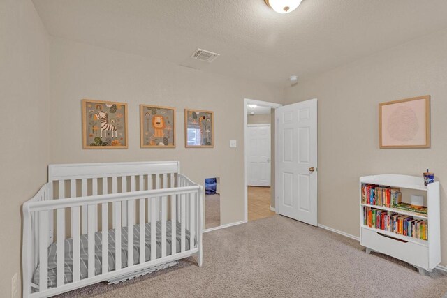 carpeted bedroom featuring visible vents, a crib, a textured ceiling, and baseboards